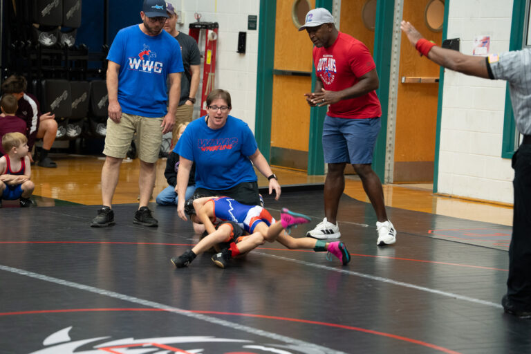 WWC coaches watching a match from the edge of the mat