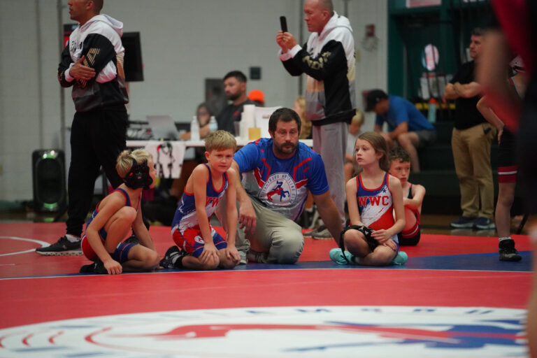 WWC wrestlers and coaches watching a match from the mat