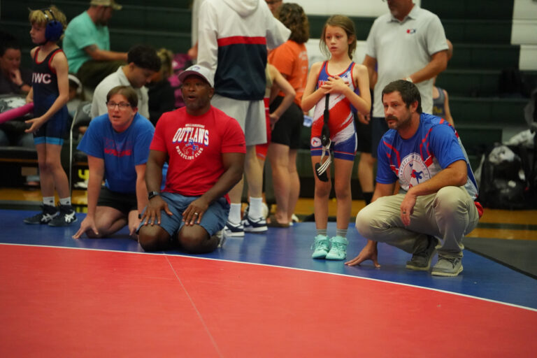 Coaches and wrestlers kneeling at the edge of the mat